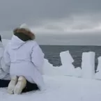 Two Inuit kneel on ice floe and look at the sky